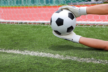 Goalkeeper's hands catching soccer ball over the line of goal wi
