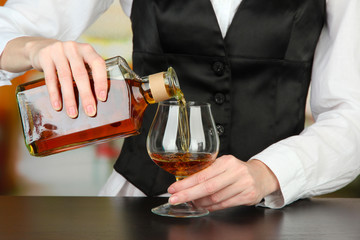 Barman hand with bottle of cognac  pouring drink into glass,