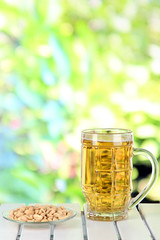 Beer in glass and nuts on table on nature background