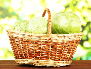Green cabbage in wicker basket, on bright background