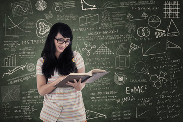 Asian female student reading book on chalkboard background