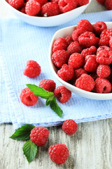 Ripe sweet raspberries in bowls on wooden background