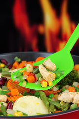 Casserole with vegetables and meat on pan, on fire background