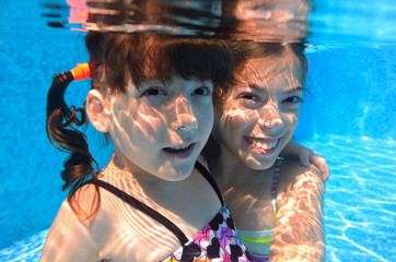 Obraz na płótnie Canvas Happy girls swim underwater in pool and having fun