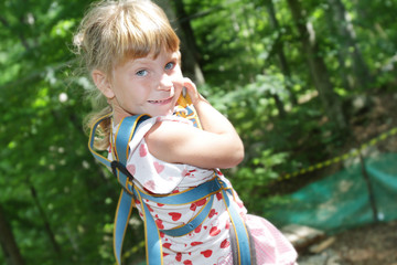 young happy child girl in adventure park in safety equipment
