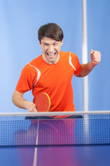 I won! Happy young men gesturing with a table tennis racket in h