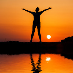 Fototapeta premium Silhouette woman jumping against orange sunset