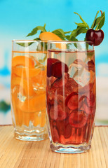 Glasses of fruit drinks with ice cubes on blue background