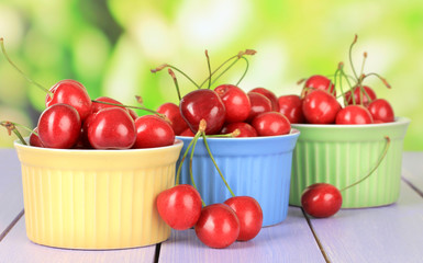 Cherry berries in bowls on wooden table on bright background