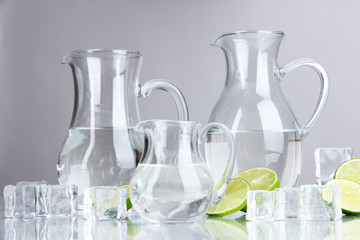 Glass pitchers of water with ice and lime on grey background