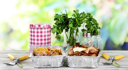 Food in boxes of foil on wooden table on nature background