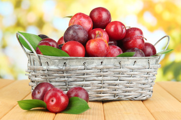 Ripe plums in basket on wooden table on natural background