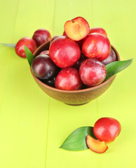 Ripe plums in bowl on wooden table close-up