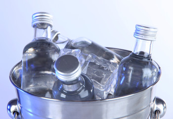 Minibar bottles in bucket with ice cubes, isolated on white