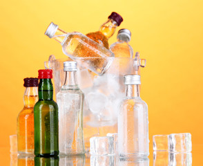 Minibar bottles in bucket with ice cubes,  on color background