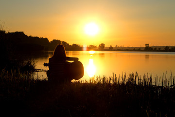 lonely romantic girl by the river playing guitar