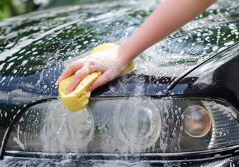 Female hand with yellow sponge washing car