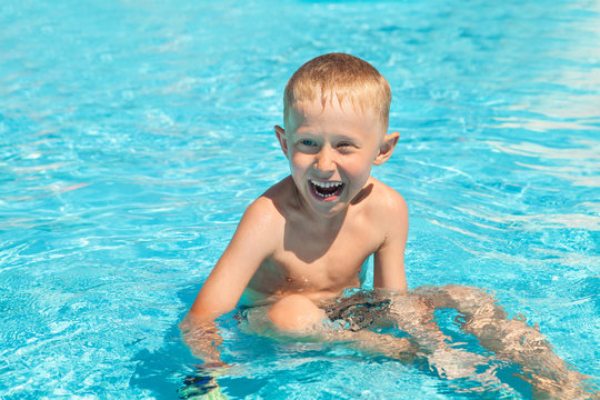 Emotional smiling little boy sitting into the pool