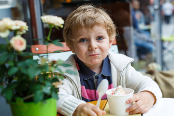 Fototapeta premium Adorable little boy eating frozen yoghurt ice cream in cafe