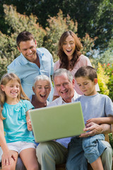 Fototapeta na wymiar Happy multi generation family with a laptop sitting in park