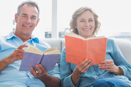 Relaxed Couple Reading Books On The Couch Smiling At Camera