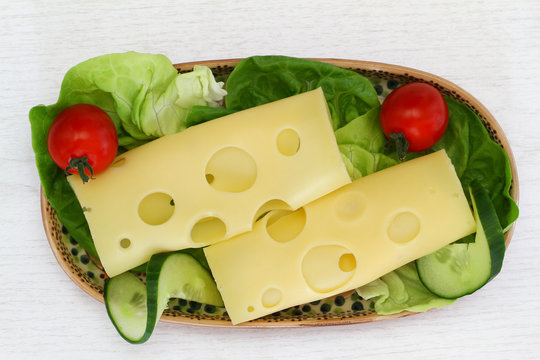 Swiss cheese on lettuce leaves with cherry tomatoes and cucumber