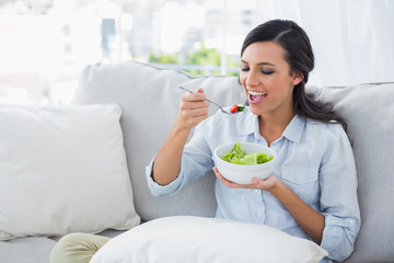 Obraz na płótnie Canvas Happy woman relaxing on the sofa eating salad