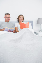 Obraz premium Smiling couple sitting in bed reading books