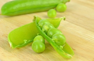 An open pea pod with peas on a wooden board