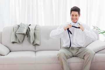Smiling businessman sitting on sofa loosening his tie