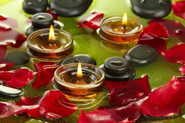spa stones with rose petals and candles in water on plate