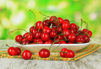 Cherry berries on plate on wooden table on bright background