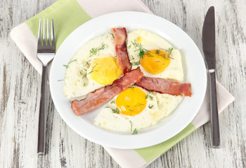 Scrambled eggs and bacon on plate on napkin on wooden table