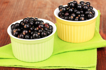Fresh black currant in bowls on napkin on wooden background