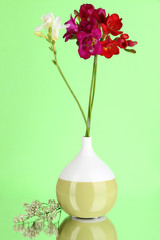 Beautiful bouquet of freesia in vase on green background