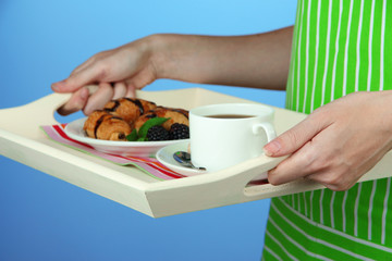 Woman in green apron holding wooden tray with breakfast,