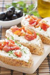 Crostini with cottage cheese, parsley and tomato on cutting boar