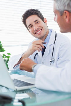 Smiling doctors talking together about something on their laptop