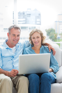 Smiling couple sitting on their couch using the laptop