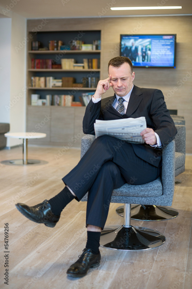 Wall mural serious businessman in suit and tie reading newspaper