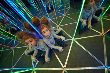 Little girl sits at crossing in mirror labyrinth illuminated