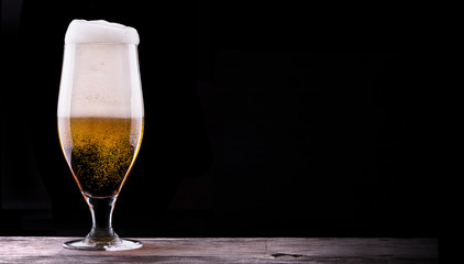 Frosty glass of light beer on black background