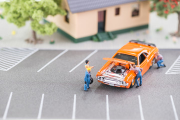 Miniature mechanics working on a car with hood up