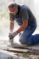 bearded man with glasses and gloves sawing stone with grinder