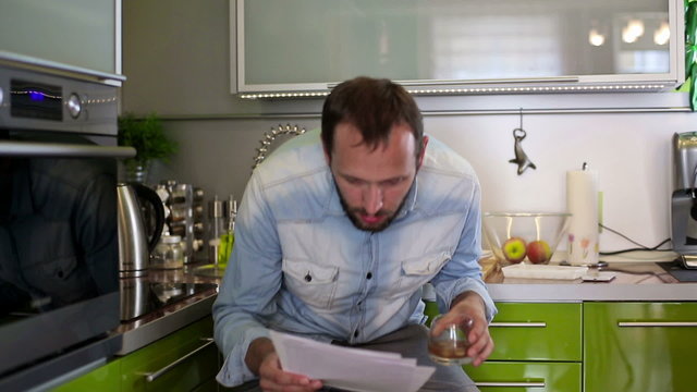 Sad, shocked man reading bills with bad news in kitchen