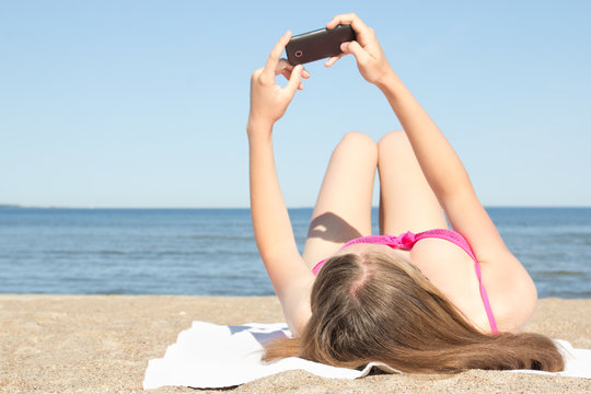young woman photographing herself with mobile phone on the beach