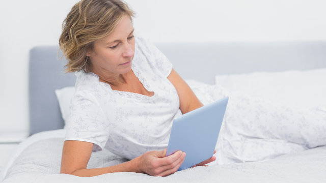 Happy blonde woman lying on bed using tablet pc