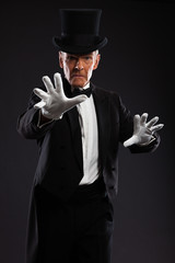 Magician making mysterious gestures. Wearing black suit and hat.