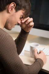 Fototapeta premium Tired man. Rear view of tired men sitting at his work place with