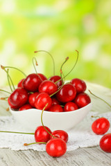 Cherry berries in bowl on wooden table on bright background
